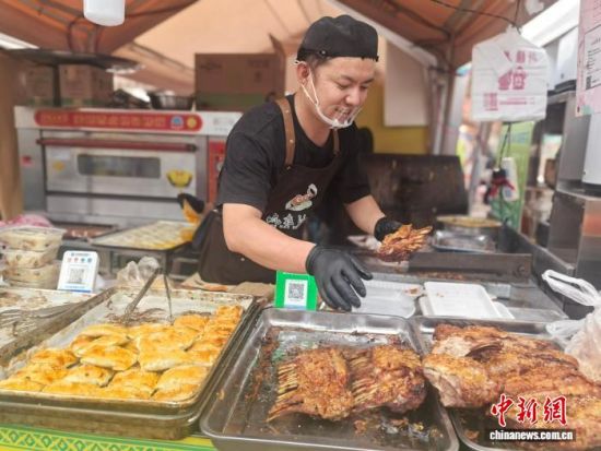 图为来自新疆伊犁的鲜先生在“吃在沙甸”美食街为顾客打包烤羊排。李艾蓉 摄 图为来自新疆伊犁的鲜先生在“吃在沙甸”美食街为顾客打包烤羊排。李艾蓉 摄